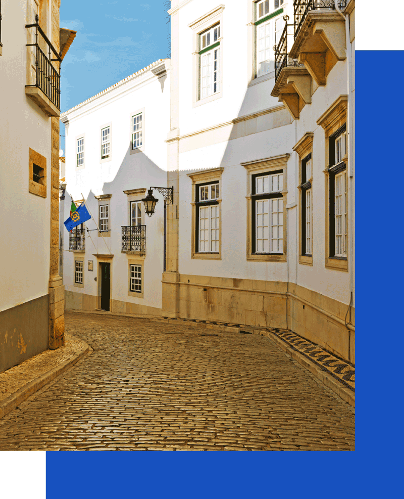Sunlit cobblestone street with white buildings.