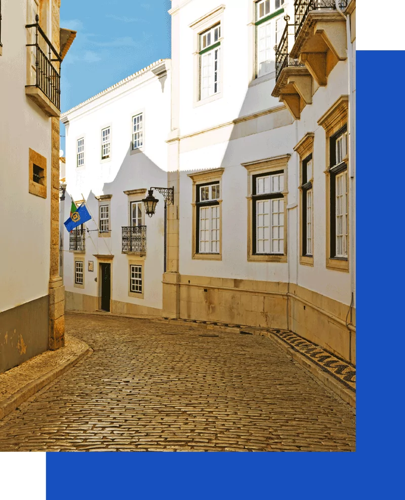 Sunlit cobblestone street with white buildings.